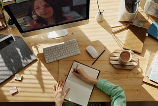 Overhead view of a person writing in a journal at a desk with a computer on it