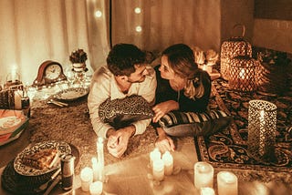 A smiling man and woman gaze into each other’s eyes in a candlelit room.