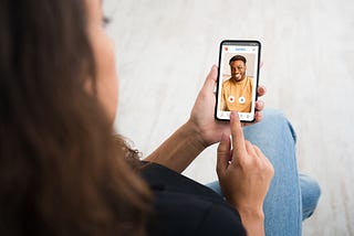 Back view over the shoulder of girl using online dating app or website, looking at male profile, touching screen