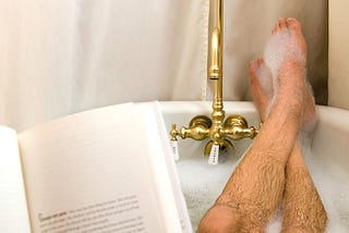 Man’s hairy legs, bubble bath, brass faucet, book