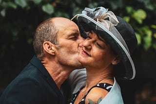 Photo of a man kissing a woman who’s wearing a hat and has her eyes closed.