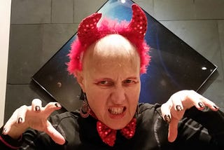 CJ Grace in her 2014 Halloween costume, chemo-bald wearing a red devil costume with glittery red horns and bow tie plus long black fake nails.