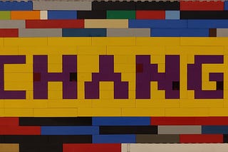 Sign made of multicolored Lego bricks with the word CHANGE in purple on a yellow background.