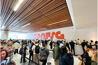 Config Registration Line with people waiting, Config rebranded logo in the center back wall behind the registration desks.