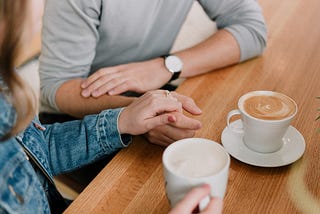 Couple holding hands with some yummy looking mugs of coffee.