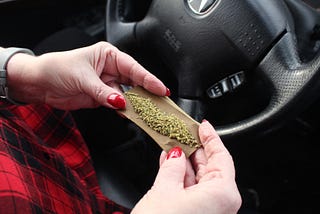 Person rolling a joint behind the steering wheel of a car.