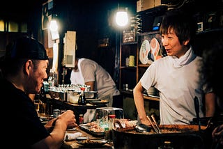 A restaurant bar with a server and a guest talking to each other