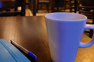 mug of coffee on a table with a notebook and pen