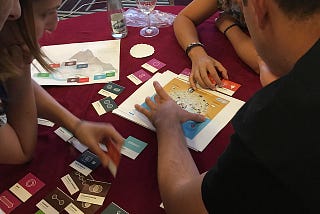 A group of people gathered around a table, interacting with tiles and printed pages.
