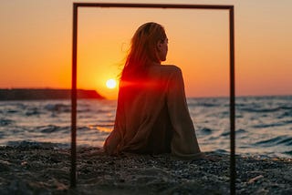 A woman on a beach at sunset, in front of a post and lintel frame, You are what you believe that you are.