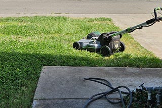 photo of lawn mower on patch of lawn next to driveway
