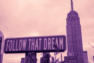 A street sign saying “FOLLOW THAT DREAM” in all caps sits in the foreground with the Empire State Building in the background just to its right.