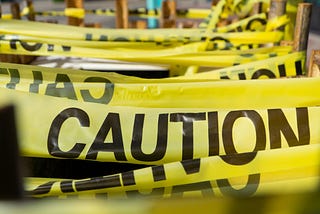 Rows and rows of yellow CAUTION tape wrapped around and around. “CAUTION” takes up most of the foreground, and the tape (some of it seen from reverse) is visible throughout the background.