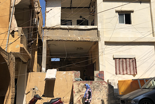 A woman in a headscarf walks past a dilapidated building.