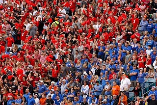 A stadium with fans wearing blue shirts in one section standing next to a section with fans all in red.