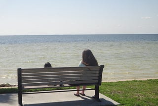 woman sitting on a bench overlooking the water while meditating.