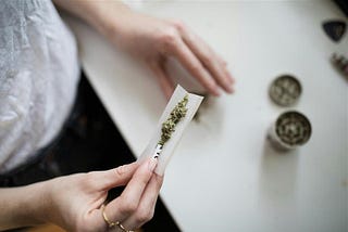 A hand holding a rolling paper with marijuana. The anonymous person is about to roll a joint.