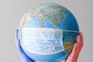 Two gloved hands holding a globe with a mask on