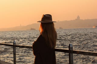 A woman stands alone at sunset looking out across the water, reflecting on the quiet freedom and peace she has built for herself.