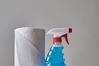 a clear bottle of blue cleaning spray next to a roll of paper towels