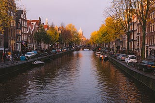 One of the many canals in Amsterdam lined with cars, gabled houses, and trees