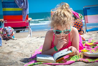 A young girl reads a book on the beach