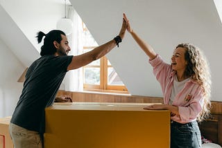 A Couple — man and woman — high fiving one another while moving a box