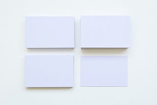 Four Stacks Of Plain Sized White Business Cards Against A White Background.