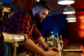 Bearded bartender wiping the bar — “A Christian and an Atheist Walk Into a Bar” by “Arthur G. Hernandez”