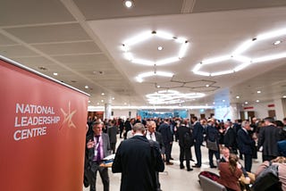 A photograph of people networking at an NLC event, with a banner in the foreground saying “National Leadership Centre”