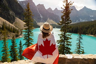 a woman draped in a canadian flag overlooking a lake and mountains