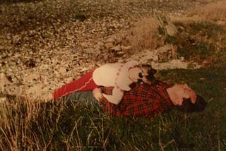 A photo of the author as a child, lying on top of her Dad, in the grass.
