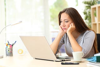A dark-haired woman with her face in her hands, looking frustrated at her computer.