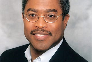 Photo of a smiling middle aged man in a shite shirt and jacket.
