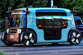 Light blue Zoox autonomous vehicle on road.
