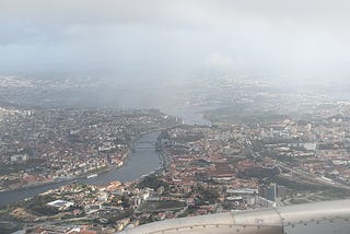 View of Porto through the fog from the airplane window. You can see River Douro, several bridges, and the red roofs of buildings.
