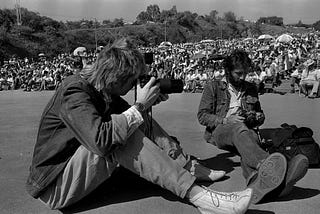 Two men sitting looking through their cameras.