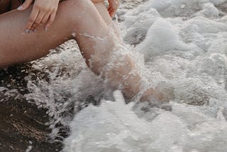 Woman with her legs in the ocean, at the beach.