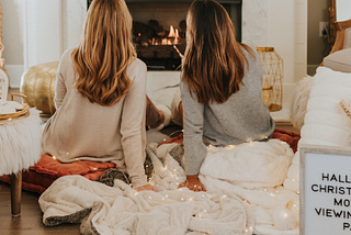 2 women watching cheesy Hallmark and Netflix Christmas movies by the fireplace during the festive holiday season.