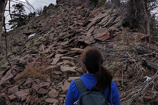 A girl standing at the bottom of a rocky part on a hike.