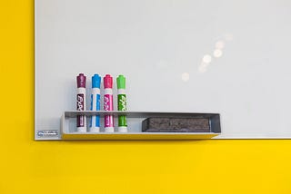 Four markers leaning against a whiteboard