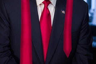 a person in a dark suit with a red tie, and the tie is very long