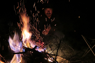 Man sitting at a beautiful campfire with an empty chair next to him