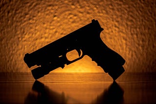 The silhouette of a handgun against an orange background.