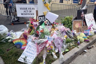 A memorial for O’Shea Sibley located at the Mobil gas station at 1935 Coney Island Ave., where he was murdered. The memorial contains many bouquets of flowers with signs behind them that appear to contain lettering that call for the end of bigotry and hatred. There is one sign that clearly reads, “Vogue as an act of resistance.” There is also a picture of Sibley.