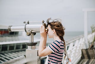 Woman using binoculars by the sea