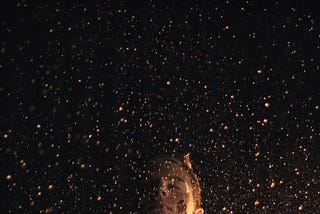 A person standing in front of a black background with gold flecks falling around them.