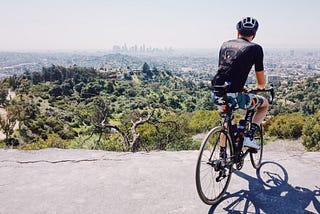 A cyclist poses at the Griffith Park Helipad, which overlooks the skyscrapers of downtown Los Angeles