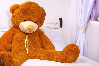 Lonely giant teddy bear sitting forgotten on a child bed | unwanted gift