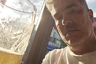Man sitting by window with half empty glass of beer in front of him.